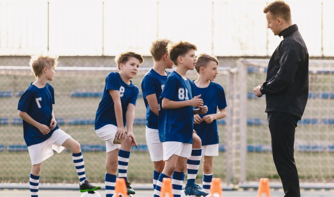 Fußballtrainer trainiert mit einer Gruppe Jungen in Fußballtrikots auf dem Fußballplatz