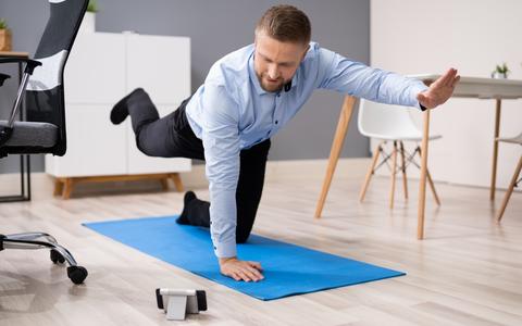 Mann macht auf Gymnastikmatte im Büro Rückengymnastik nach App