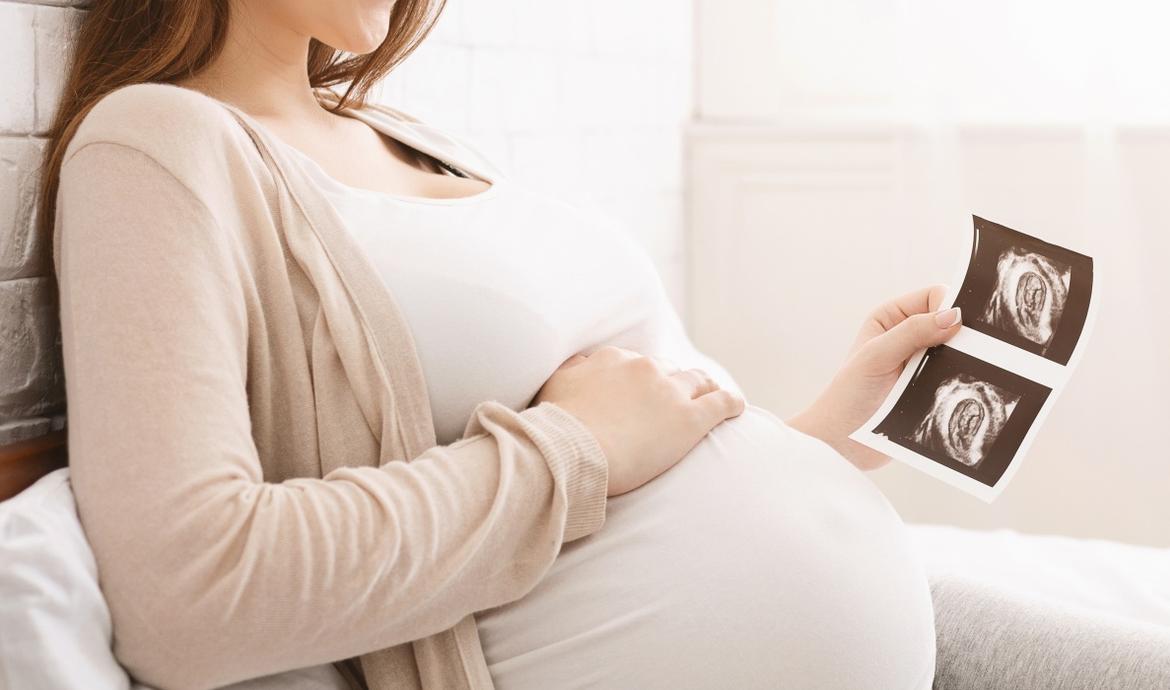 Schwangere liegt entspannt und hält Hand auf den Bauch und betrachtet Ultraschallbilder